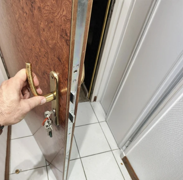 Homme manipulant une poignée de porte dorée sur une porte en bois avec mécanisme de serrure apparent, dans un intérieur carrelage blanc