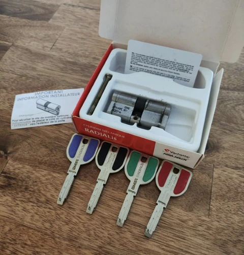 Intérieur sur parquet bois, boîtier de serrurerie ouvert contenant cylindre de sécurité et clés colorées