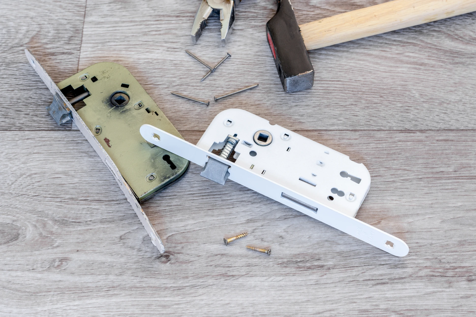 Intérieur résidentiel, individu encagoulé en sweat bordeaux forçant une serrure de porte en bois avec des outils de crochetage