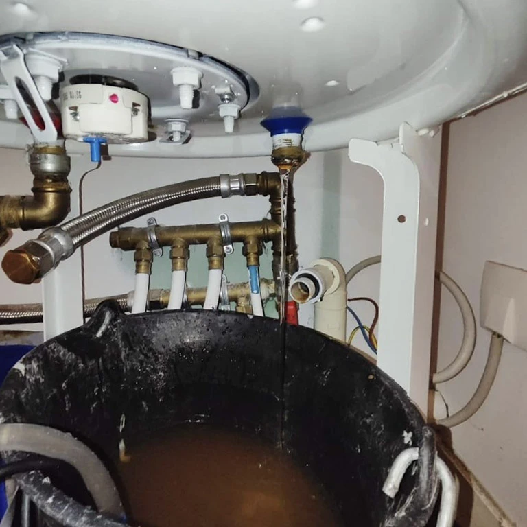 Plombier professionnel à genoux dans une salle de bain moderne, intervenant sous un lavabo blanc avec robinetterie chromée